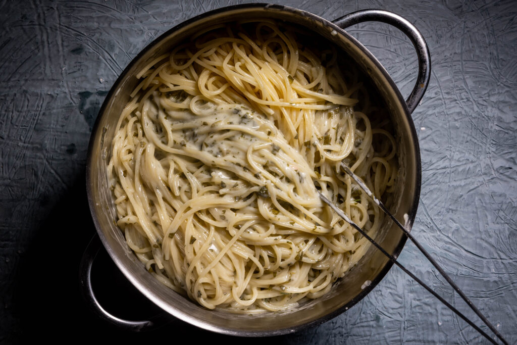 Sauerampfersauce wird in einem Topf unter heiße Pasta gehoben.