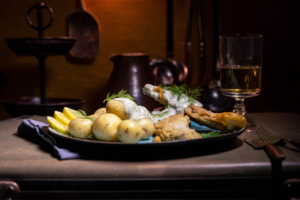 Visch mit Dillsauce und Kartoffelnauf einem Teller, der auf einem alten Koffer steht.