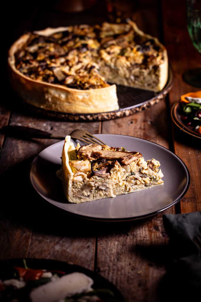 Waldpilz-Wirsing-Quiche , ein Stück auf einem Teller, dahinter die restliche Quiche.