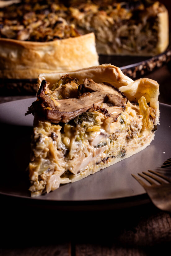 Waldpilz-Wirsing-Quiche - vegan - ein Stück auf einem grauen Teller, die restliche Quiche im Hintergrund.