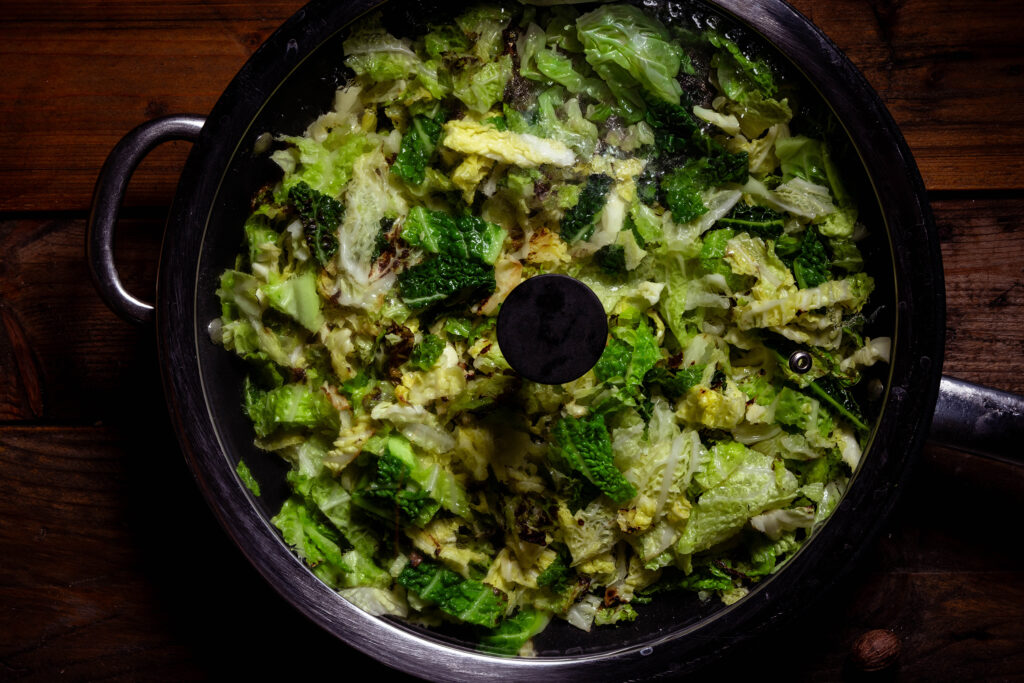 Wirsing wird in einer Pfanne mit Glasdeckel gedünstet.