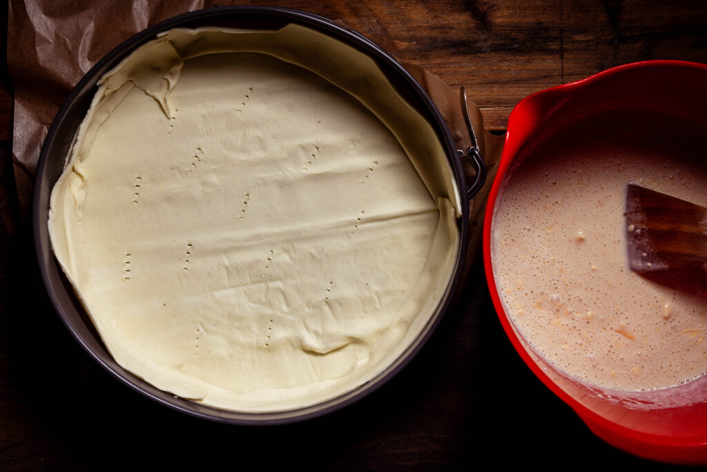 Eine Backform, ausgelegt mit Blätterteig. Eine Schüssel mit Quichfüllmasse.