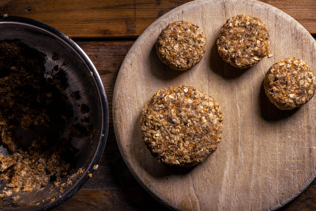 3 vegane Bouletten und ein Burgerpatty auf einem Holzbrett.