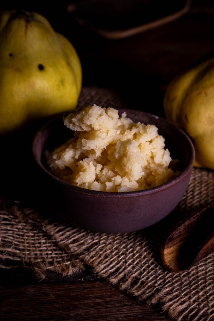 Fermentierte Quitten, püriert in einer Schale. Dahinter frische Quitten.