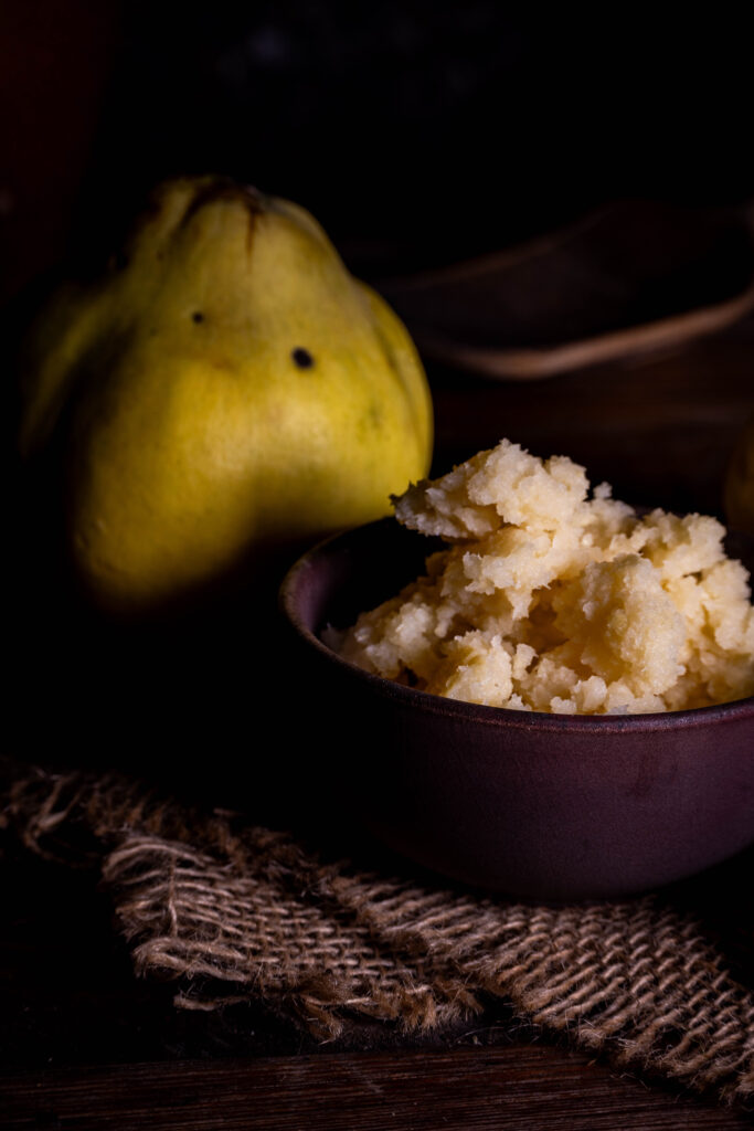 Fermentierte Quitten, püriert in einer Schale. Dahinter frische Quitten.