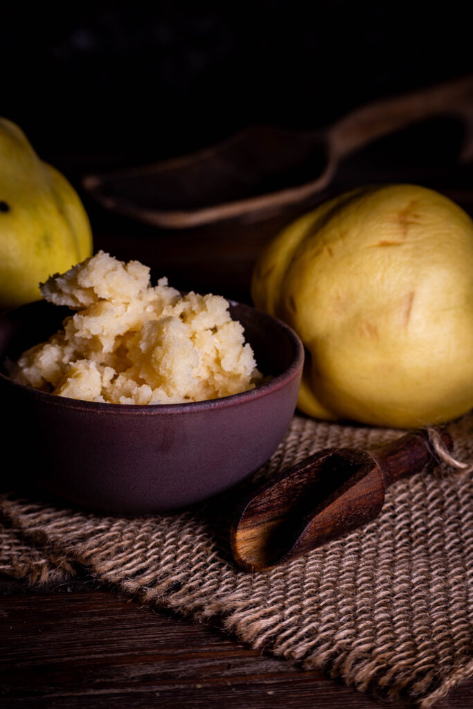Fermentierte Quitten, püriert in einer Schale. Dahinter frische Quitten.