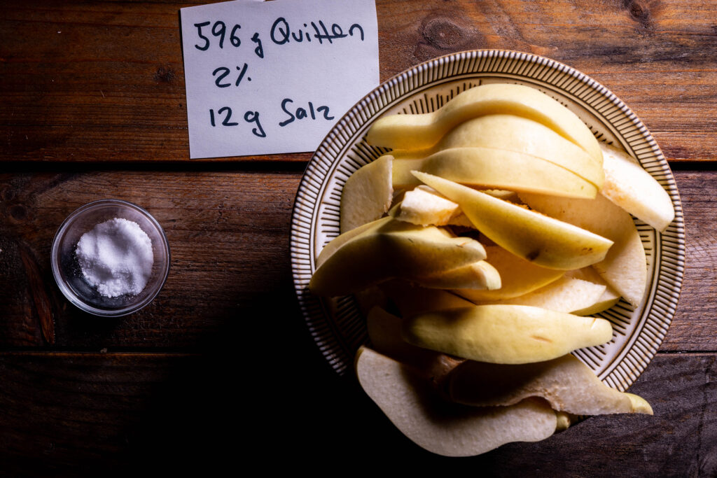 Quittenschnitze in einer Schale, eine kleine Schale mit Salz und ein handgeschriebener Zettel mit Gewichtsangaben.