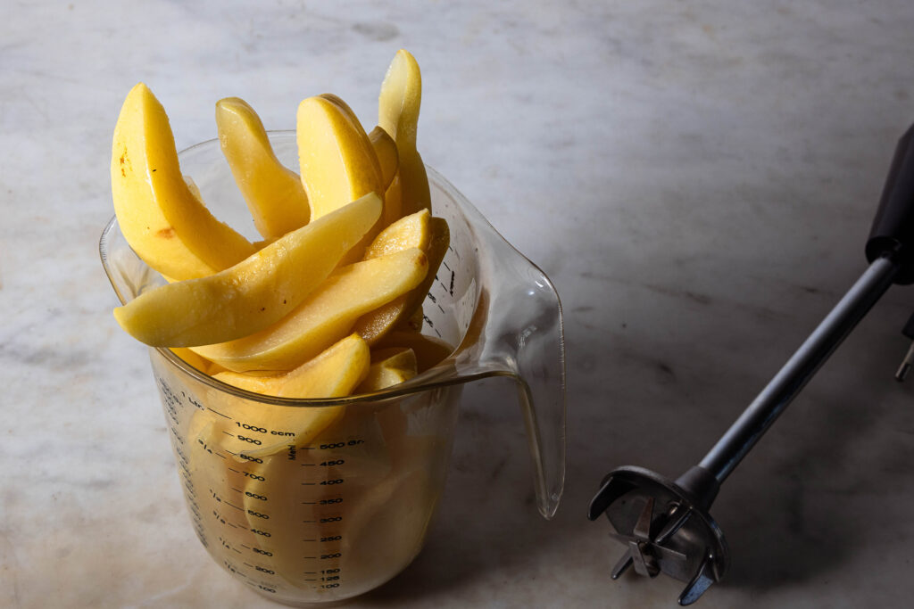 Quitten in einem Messbecher, daneben ein Pürierstab.