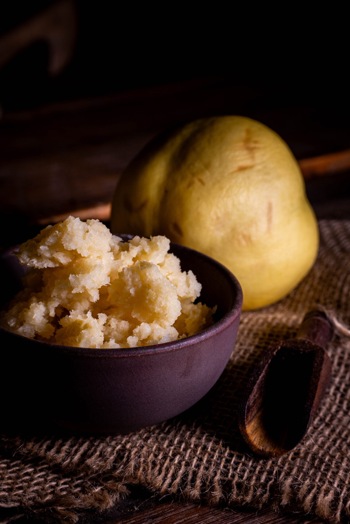 Fermentierte Quitten, püriert in einer kleinen Schale. Dahinter eine frische Quitte.