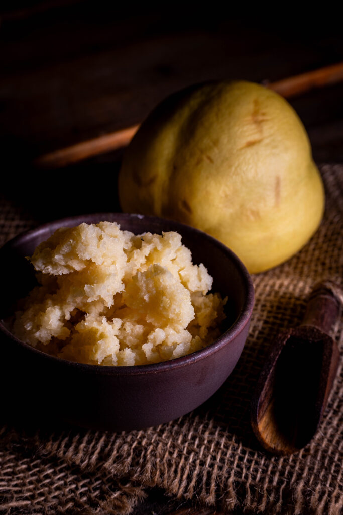Fermentierte Quitten, püriert in einer Schale. Dahinter frische Quitten.