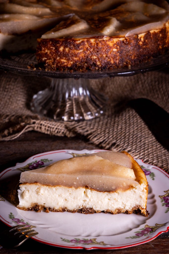Veganer Käsekuchen mit fermentierten Quitten, ein Stück auf einem Teller, der Rest des Kuchens dahinter auf einer Etagere
