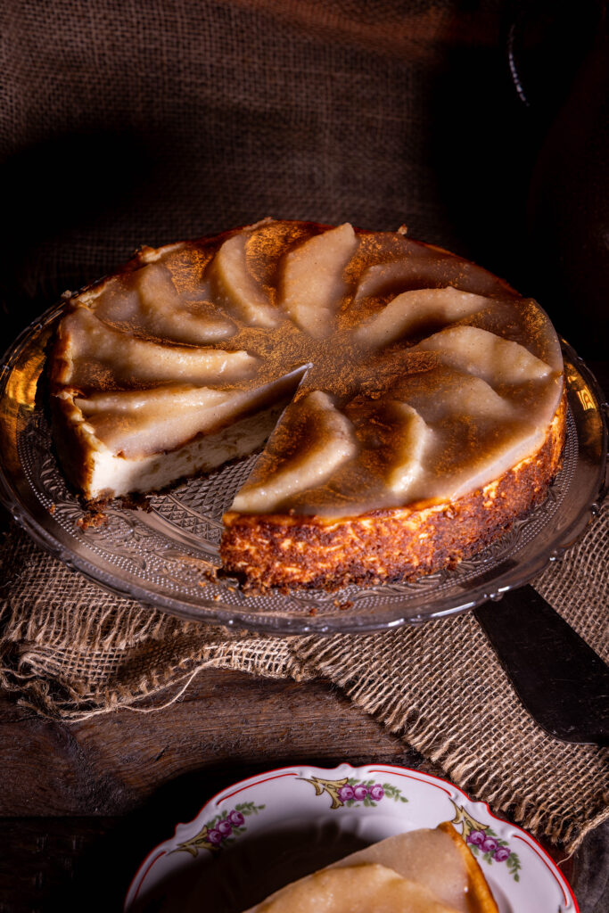 Veganer Käsekuchen mit fermentierten Quitten, ein Stück auf einem Teller, der Rest des Kuchens dahinter auf einer Etagere