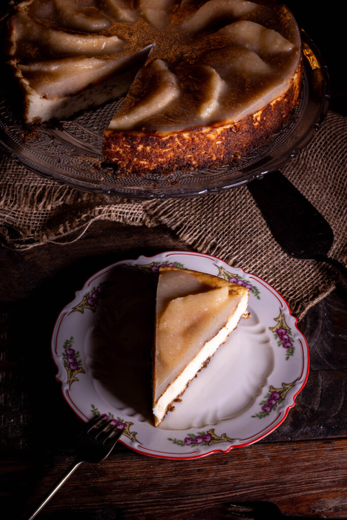 Veganer Käsekuchen mit fermentierten Quitten, ein Stück auf einem Teller, der Rest des Kuchens dahinter auf einer Etagere