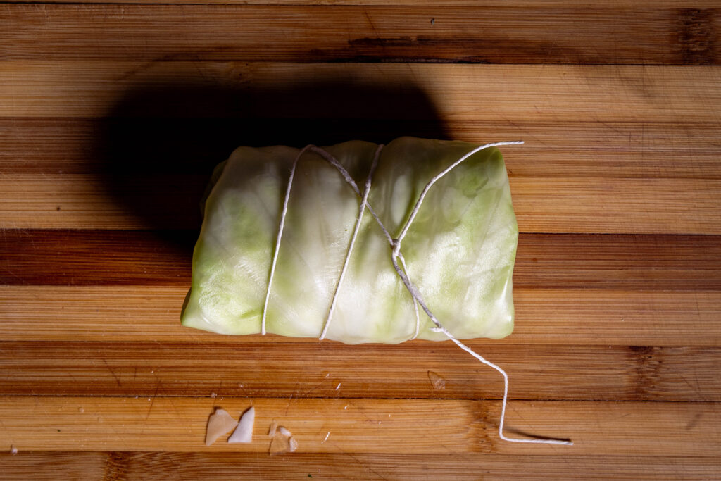 Eine rohe vegane Kohlroulade auf einem Holzbrett.