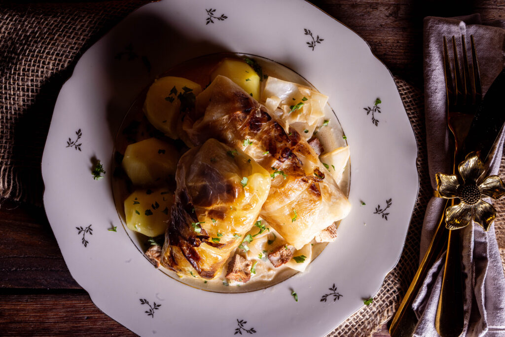 Vegane Kohlrouladen - zwei auf einem Teller, mit Kohlsauce und Petersilienkartoffeln.