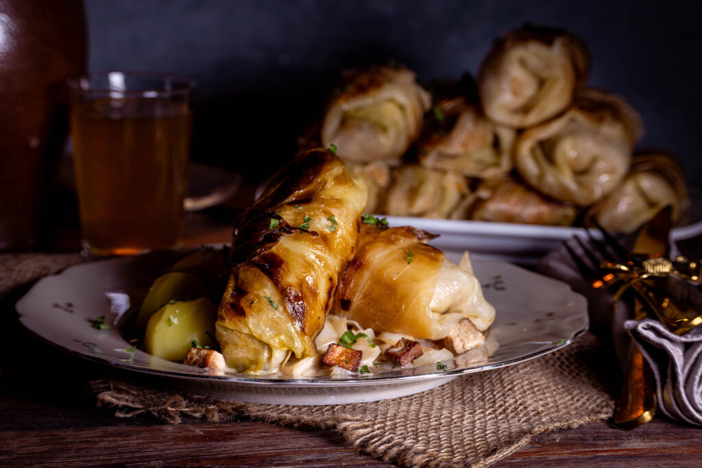 Vegane Kohlrouladen - zwei Stück auf einem Teller, dahinter eine Platte mit mehr Rouladen.