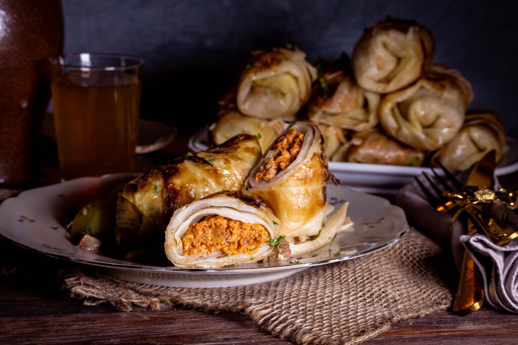 Vegane Kohlrouladen, zwei auf einem Teller, eine angeschnitten. IM Kintergrund eine Platte mit mehr Rouladen.