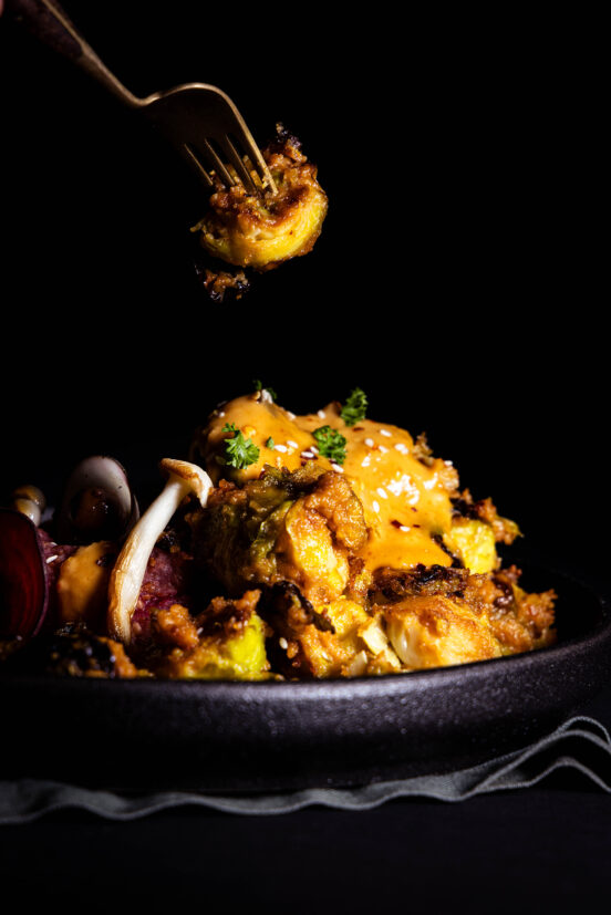 Rosenkohl in Erdnusssauce, mit Beilagen auf einem Teller und auf einer Gabel.