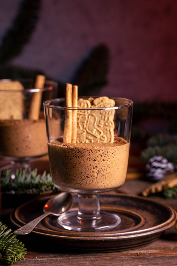 Spekulatius-Mousse in Dessertgläsern, dekoriert mit Zimtstange und einem Spekulatiuskeks. Auf einem weihnachtlichen Holztisch.