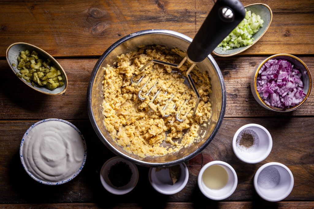 Kichererbsen werden mit einem Kartoffelstampfer fein gestampft. Außerdem weitere Zutaten für veganen ThunVischsalat.