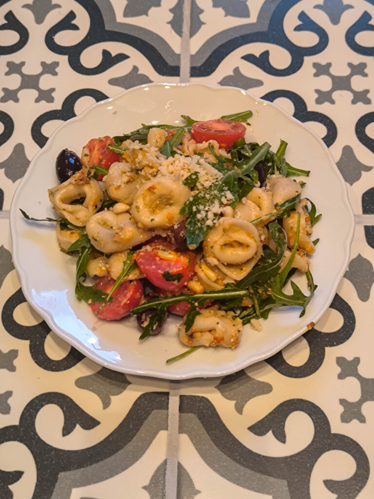 Tortellini-Salat auf einem Teller auf einem gekachelten Tisch.