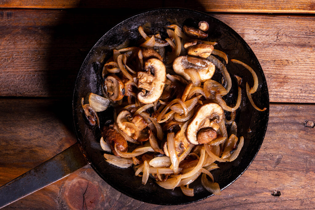 Champignons und Zwiebelstreifen braten in einer Pfanne.