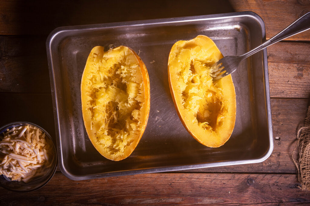 Das Fleisch von einem Spaghettikürbis wird mit einer Gabel aufgelockert.