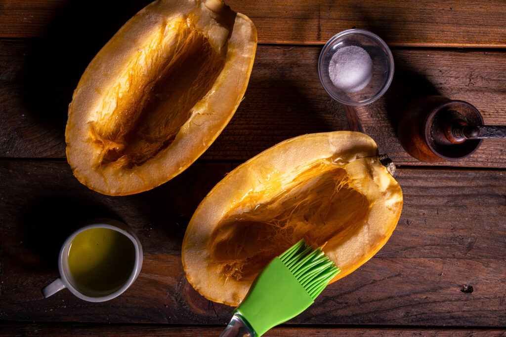 Zwei Spaghettikürbishälften, Öl, Salz, Pfeffer. Eoine Kürbishälfte wird mit Olivenöl bestrichen.