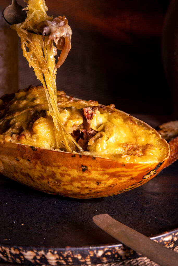 Eine Gabel holt einen Bissen aus einem mit Jackfruit-Ragout gefülltem Spaghettikürbis