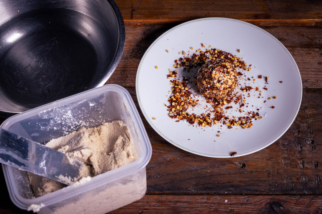 Vegane Frischekäsebällchen werden in Chiliflocken gerollt.