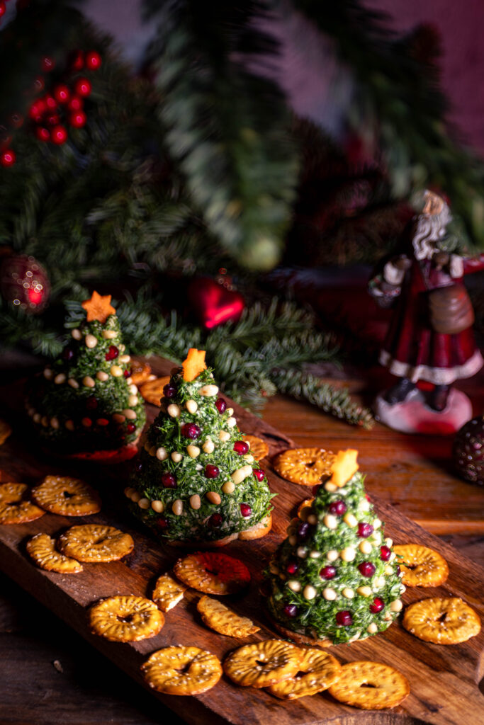 Frischkäse Tannenbäume - vegan - drei Stück mit Crackern auf einem weihnachtlich dekoriertem Holztisch.