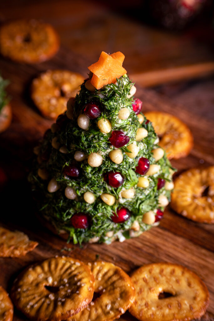 Dekoriertes Vrischkäse-Weihnachtsbäumchen mit Crackern auf einem Holzbrett.