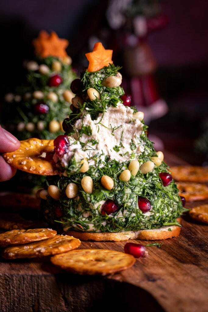 Ein Cracker wird in einen cremigen Vrischkäse-Weihnachtsbaum geteckt und bricht diesen an.