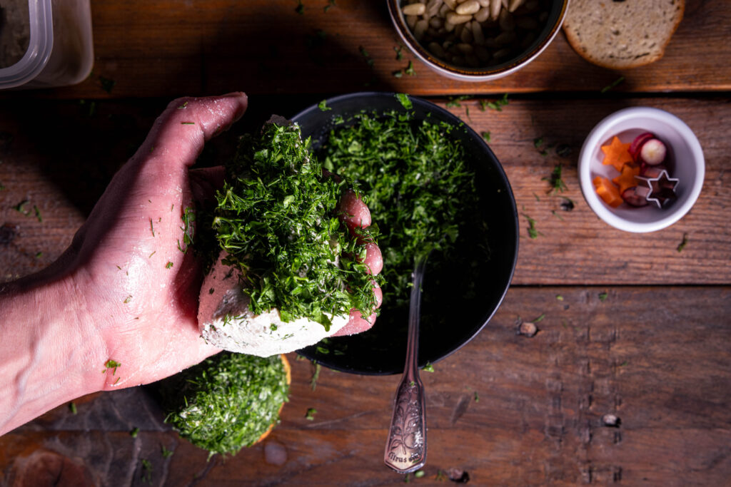 Ein Frischkäsekegel wird mit den gehackten Kräutern ummantelt.