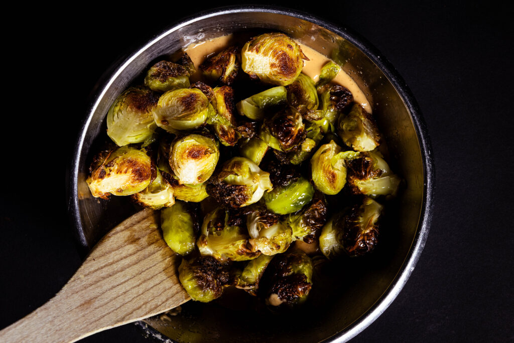 Hot Brussels sprouts are being added to a bowl with peanut sauce in it.