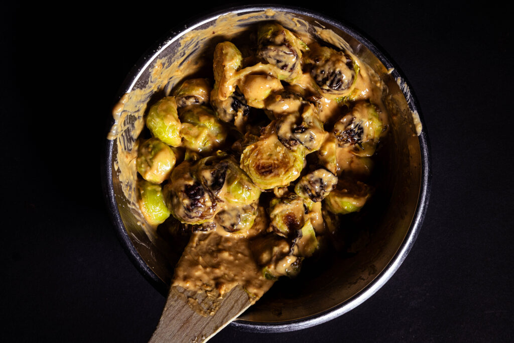 Hot Brussels sprouts are being mixed with peanut sauce in it.