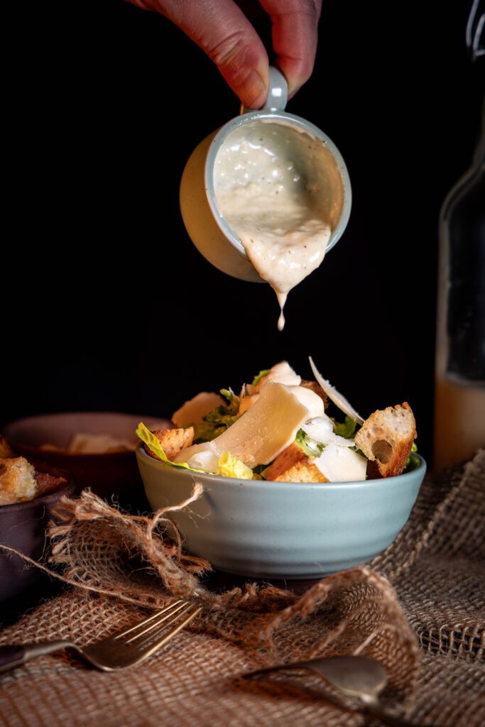 Veganes Caesar Dressing wird auf einen Salat gegeben.