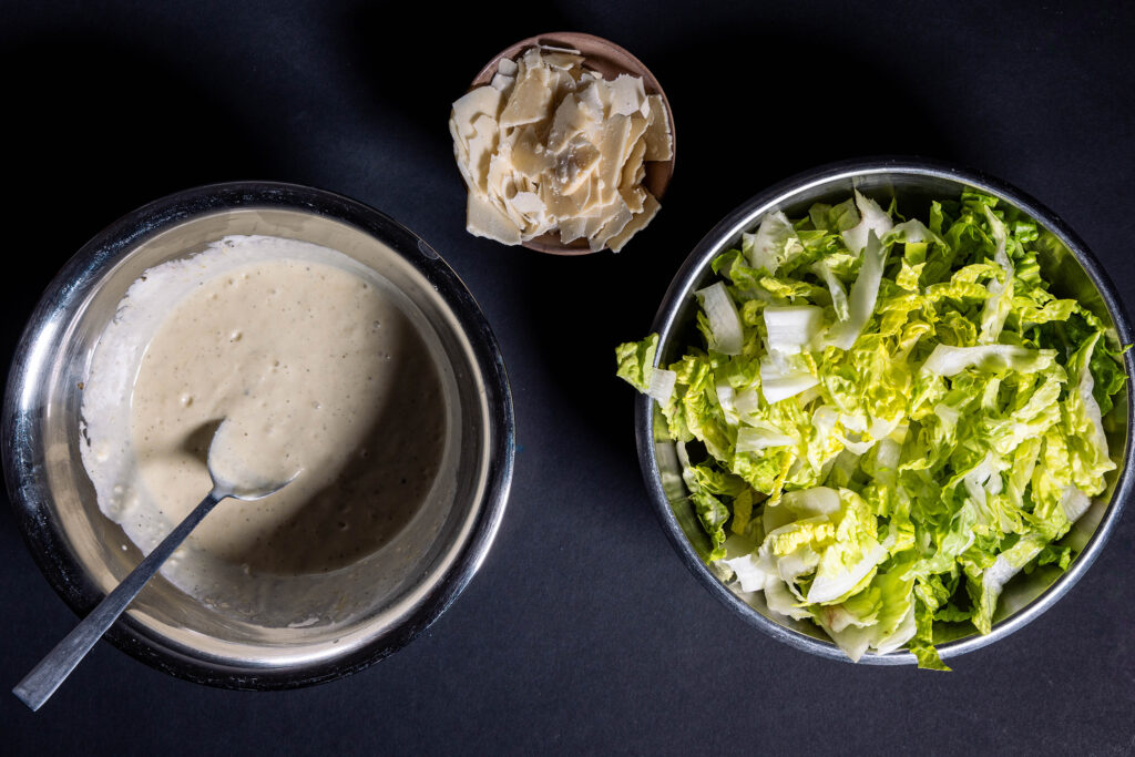 Romanasalat, das fertige Caesar Dressing und gehobelter, veganer Parmesan.