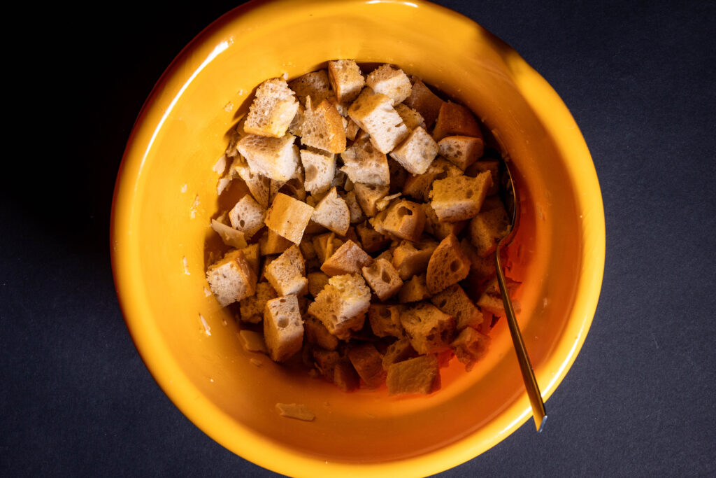 Brotwürfel werden mit weiteren Zutaten in einer Schüssel vermengt.