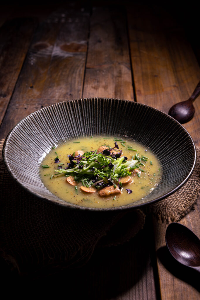 Kartoffelsuppe mit Wursteinlage - vegan, in einem tiefen Teller, daneben rustikale Holzlöffel