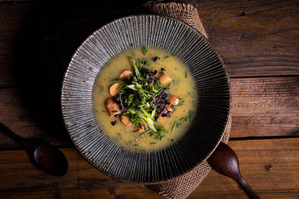 Cremige, deftige Kartoffelsuppe mit Würstchen, in Scheiben als Suppeneinlage. Darauf Lauchzwiebeln und Kräuter.