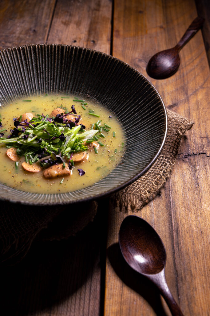 Vegane Kartoffelsuppe mit Würstchen in einem tiefen Teller auf einem Holztisch.