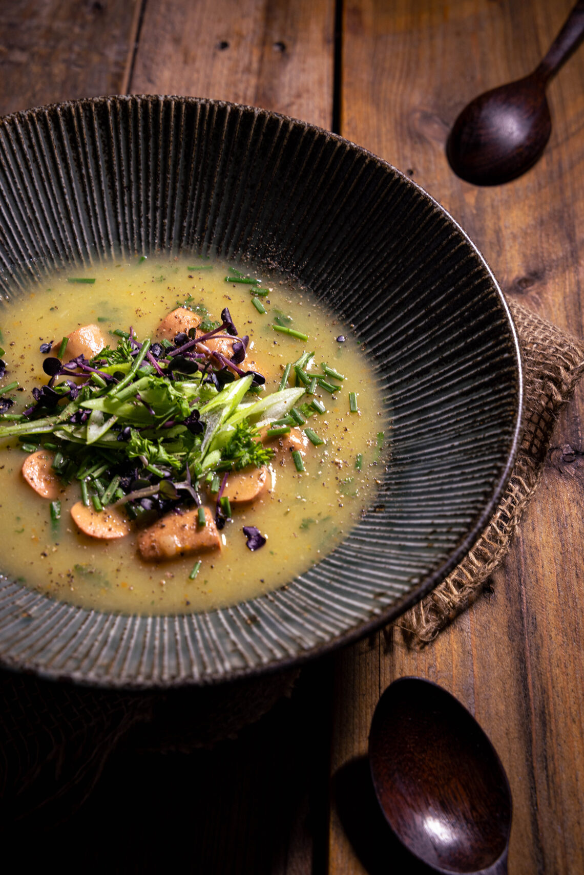 Kartoffelsuppe mit Wursteinlage - in einem tiefen Teller auf einem Holztisch