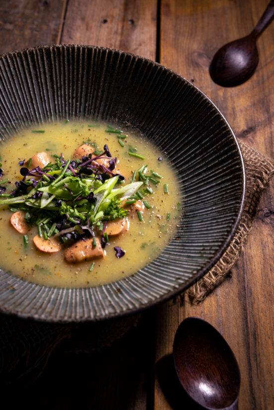 Kartoffelsuppe mit Wursteinlage - in einem tiefen Teller auf einem Holztisch