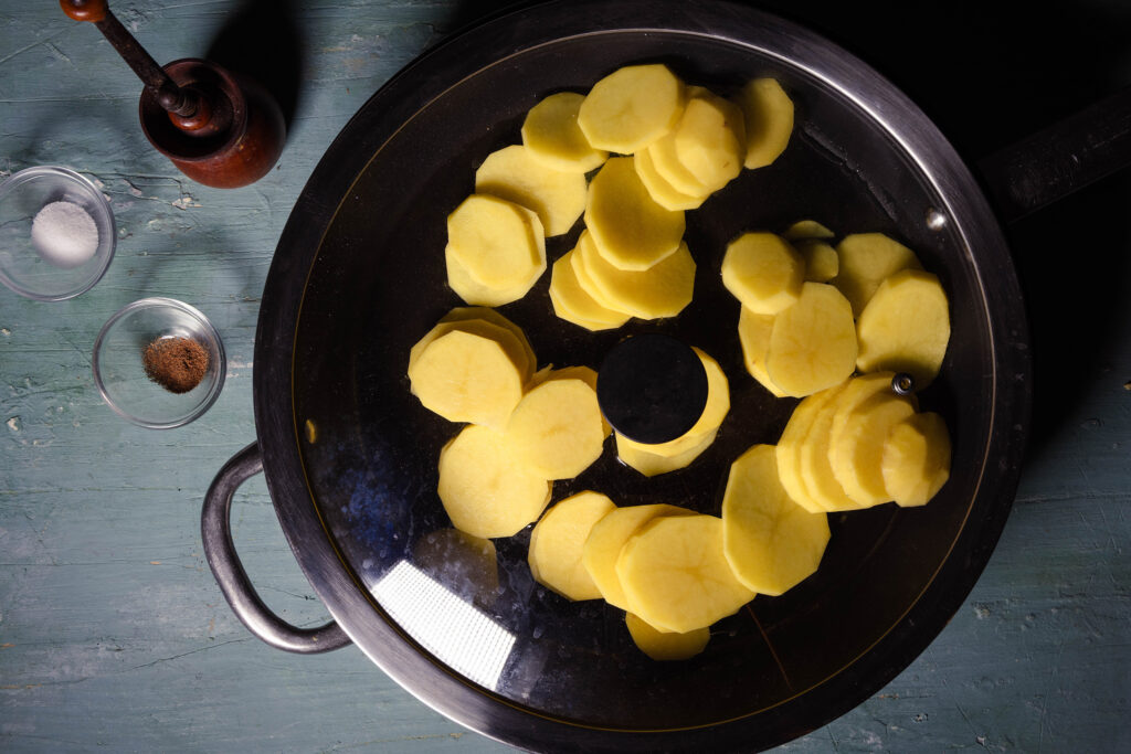 Kartoffeln in Scheiben braten in einer Pfanne mit Deckel.