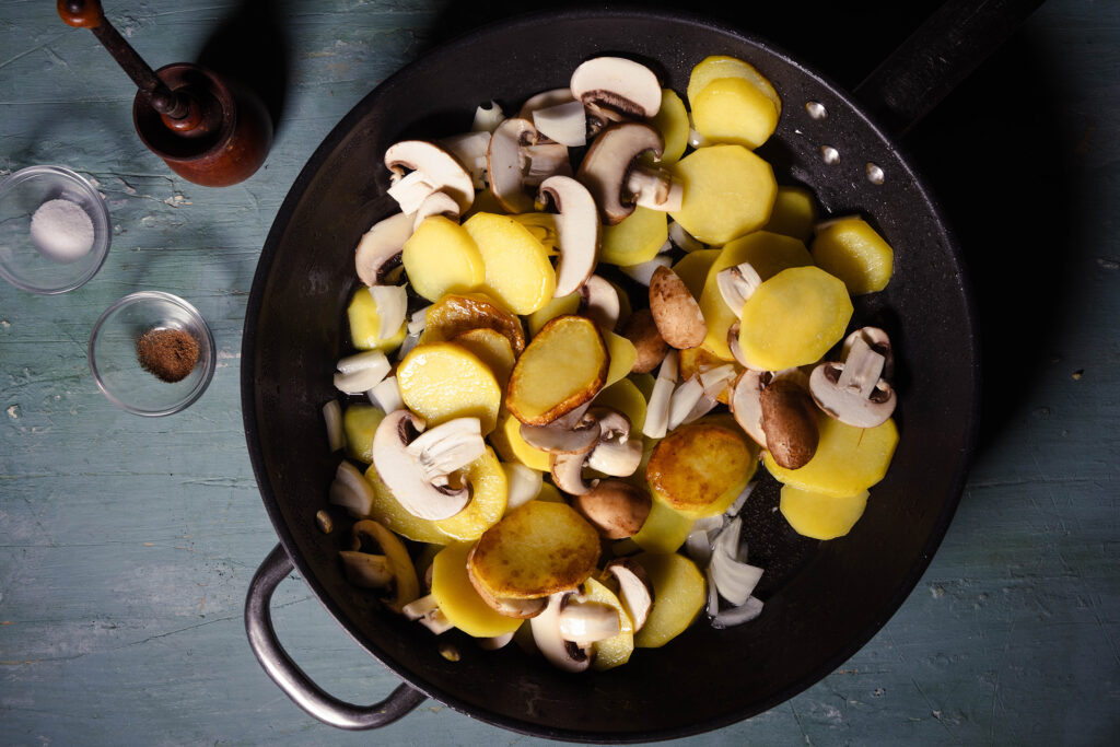 Bratkartoffeln, Champignons und Zwiebeln braten in einer Pfanne.