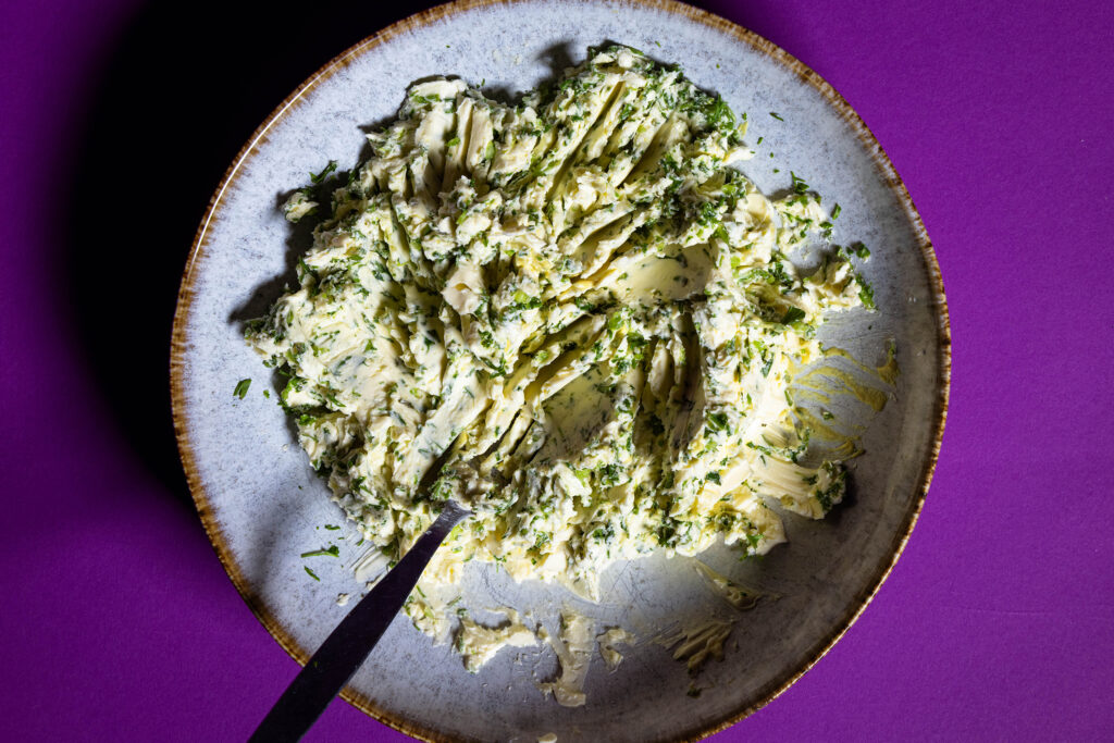 Eine vegane Kräuterbutter wird auch einem Teller mit einer Gabel angemischt.