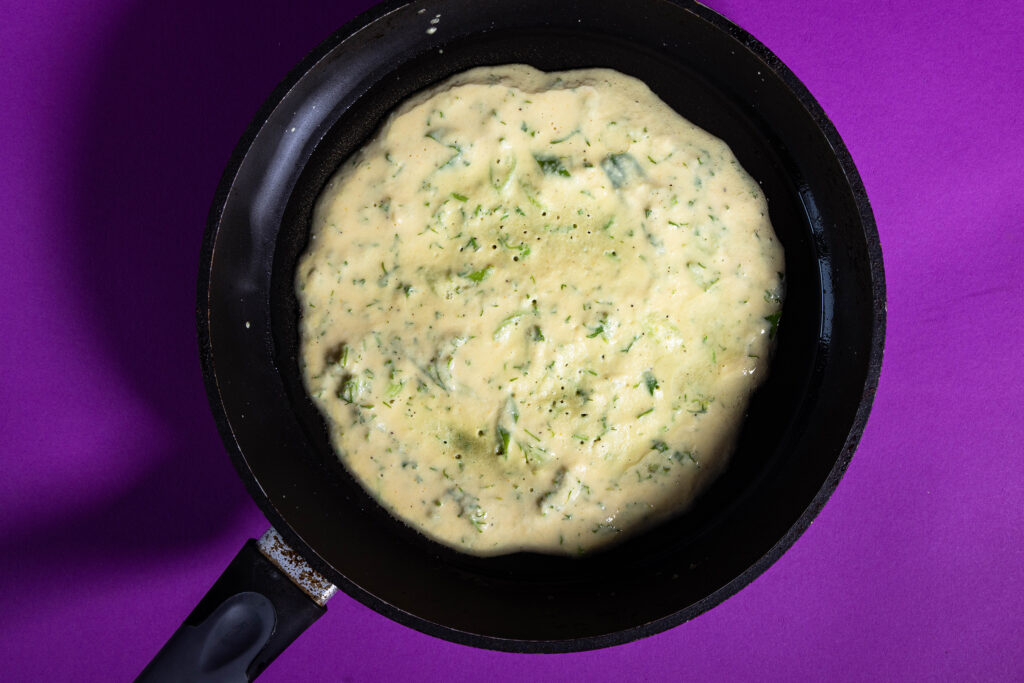 Ein veganes Blattsenf-Omelette brät in einer Pfanne.