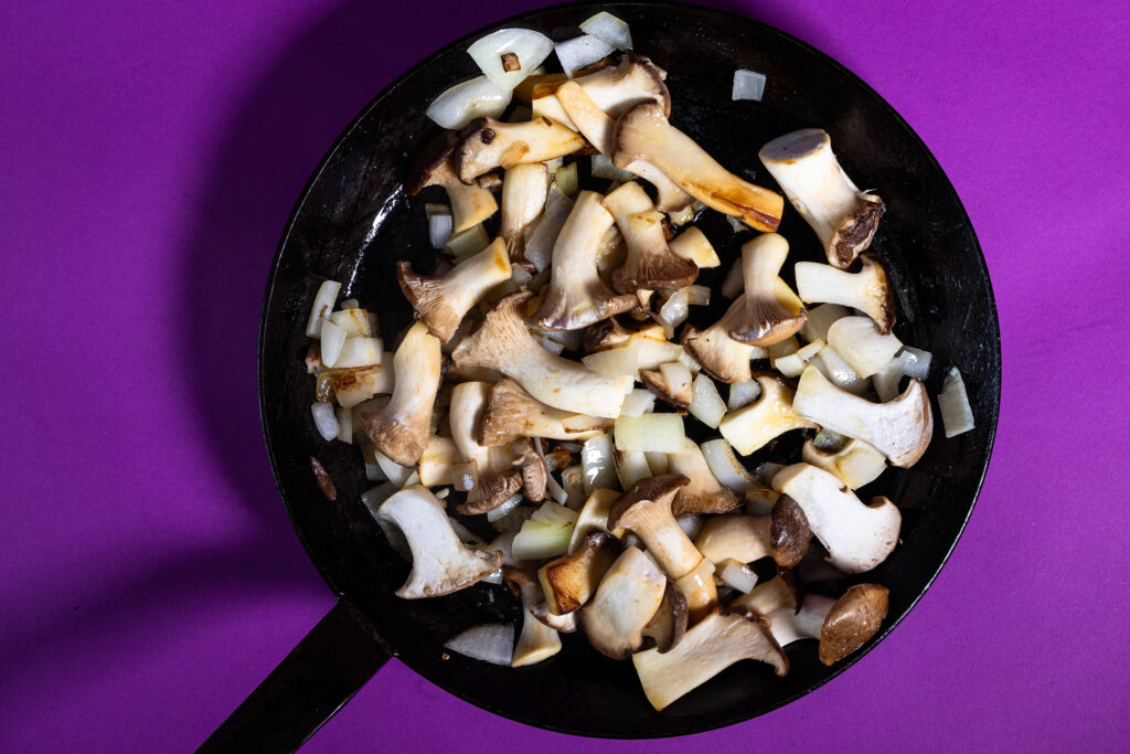 Kräuterseitlinge und Zwiebelwürfel braten in einer Pfanne.