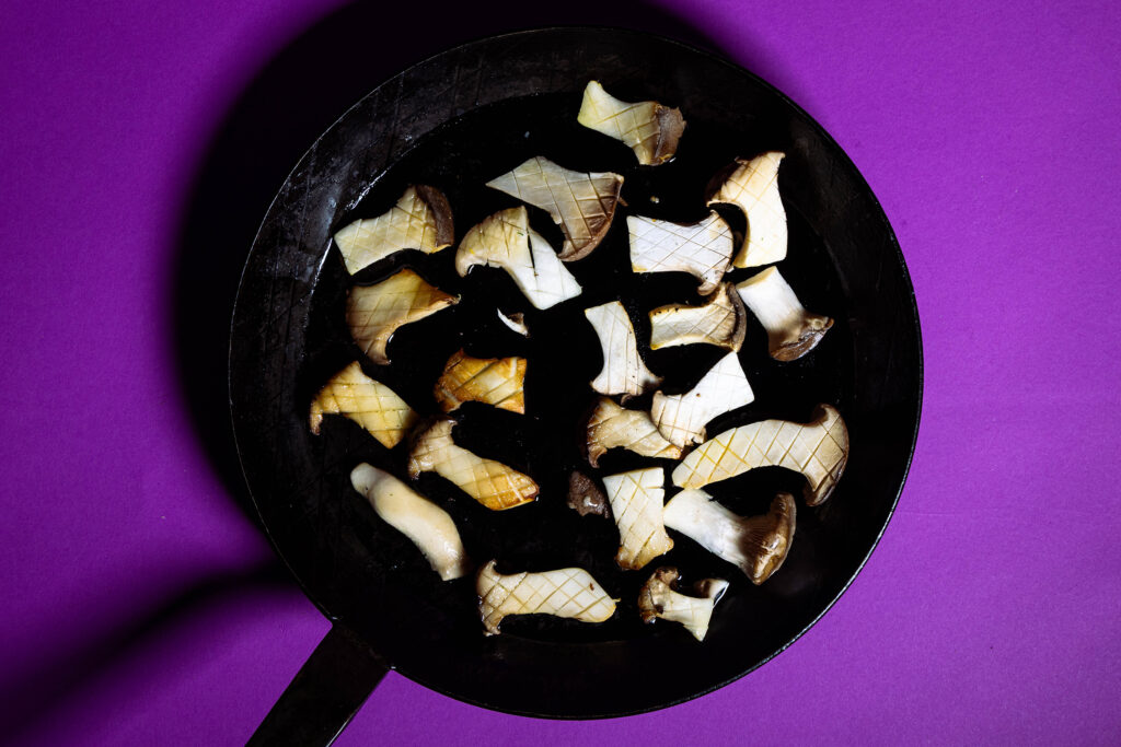 Kräuterseitlinge, in Scheiben, kreuzförmig eingeritzt, braten in einer Pfanne.